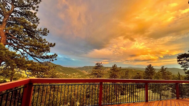 Eine Holzterrasse mit Metallgeländer, mit Blick auf eine Berglandschaft mit Bäumen und einem Sonnenuntergangshimmel.