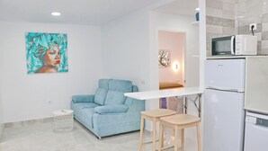 A modern living room with a blue sofa, a small round table, and a white refrigerator. - Ceuta apartment near the beach (Conil de la Frontera)