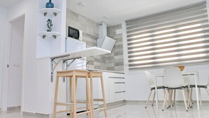 A modern kitchen with white cabinetry, a microwave, and a built-in oven. There are two wooden stools and a white dining table with chairs. - Ceuta apartment near the beach (Conil de la Frontera)