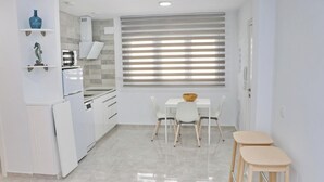 A compact kitchen with white cabinets, a built-in oven, and a dining area with a table and chairs. - Ceuta apartment near the beach (Conil de la Frontera)