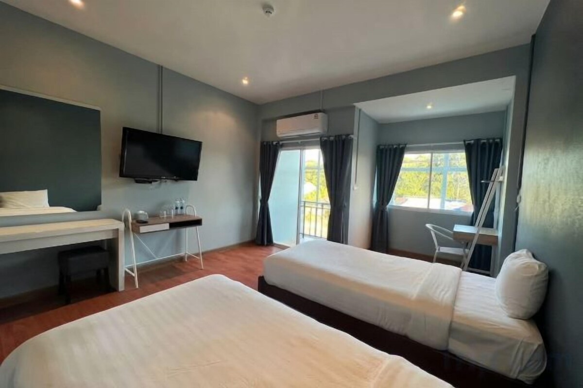 A hotel room with two beds, a desk, a television, and a window with curtains.