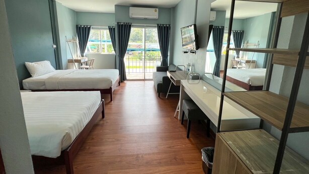 Habitación de hotel con dos camas, un escritorio, una silla, un televisor y un balcón con cortinas.