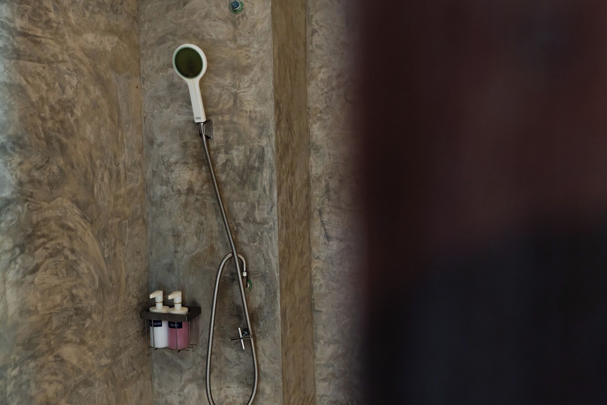 Un área de ducha con cabezal de ducha de mano y grifo empotrado en la pared.
