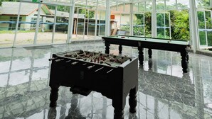 Amplio espacio interior con techo alto y ventanas grandes, que cuenta con dos mesas de futbolín y un piso de mármol pulido.