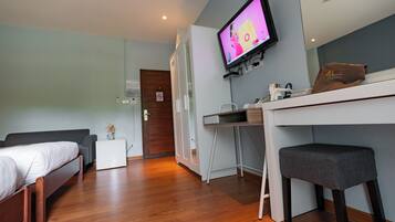 A modern hotel room with a bed, a desk, a chair, a television, and a small table with a towel.