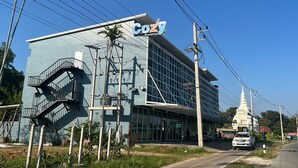 Un hotel llamado 'Cozy' con fachada de vidrio moderno, una escalera destacada y una estructura en el fondo que recuerda a un pagodas blanco.