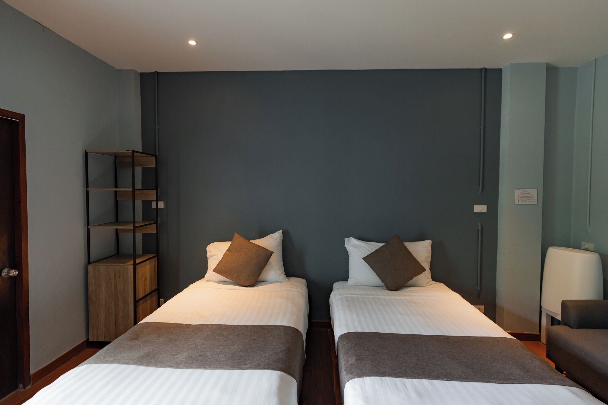 Una habitación con dos camas, una estantería de madera, una silla y una mesita de noche.