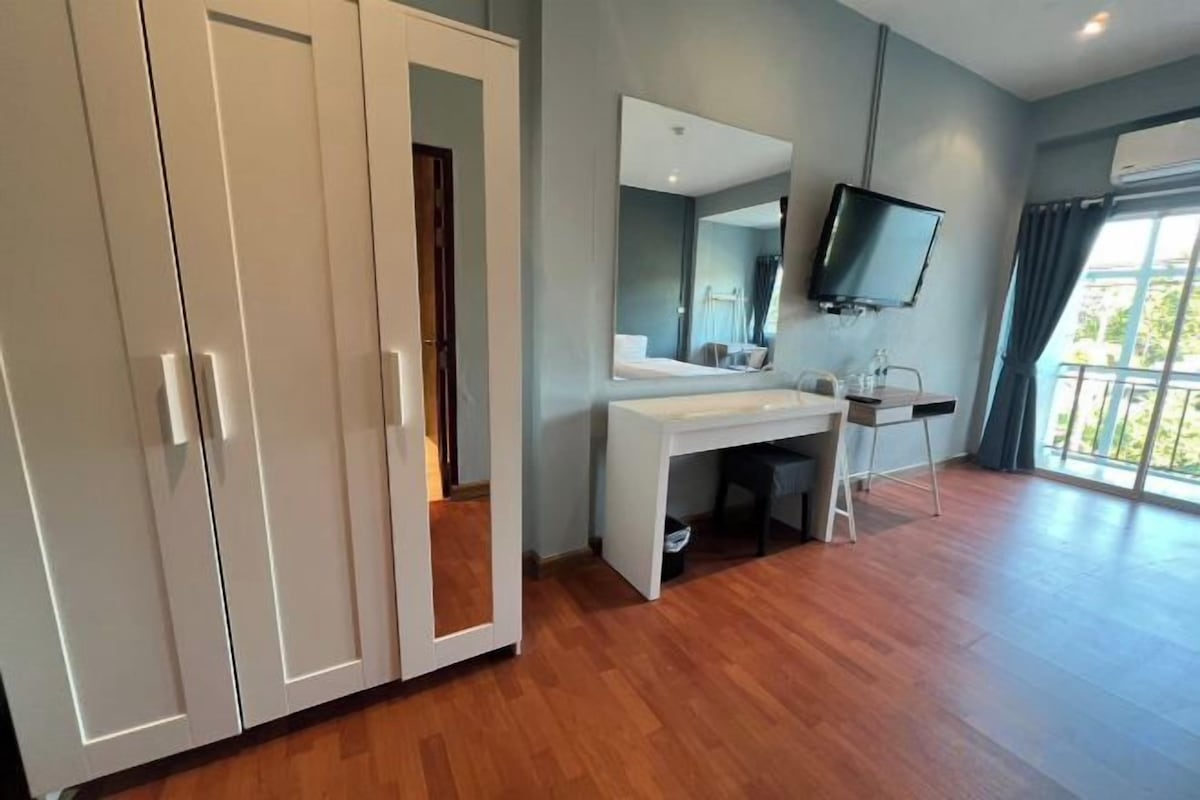Habitación de hotel con piso de madera, un escritorio blanco, un espejo, un televisor y un armario.