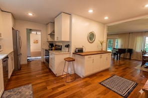 A modern kitchen with a wooden countertop, white cabinets, and a central island with stools. - Stunning Ranch in the woods! (Berrien Springs)