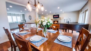 A dining area with a wooden table set for six, surrounded by chairs, with a vase of flowers in the center. - Stunning Ranch in the woods! (Berrien Springs)
