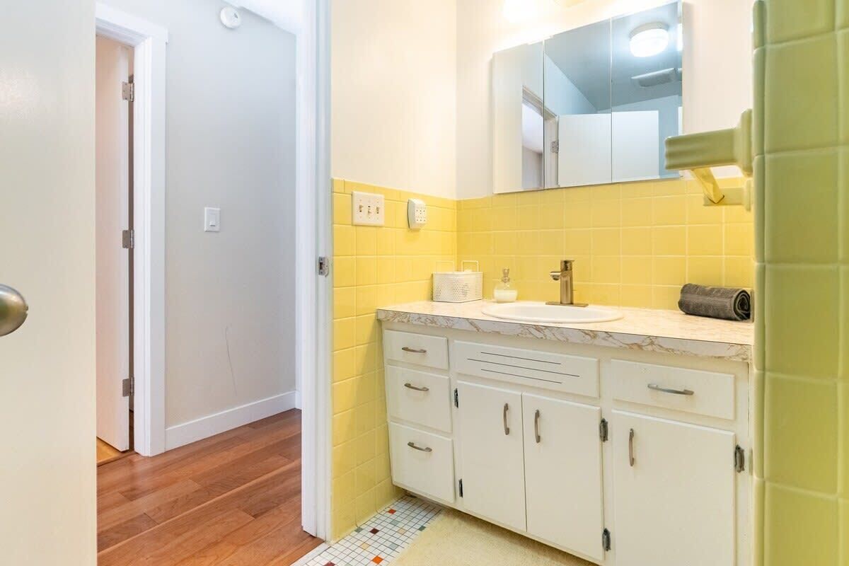 A bathroom with a white sink, yellow-tiled walls, and a mirror above the sink.