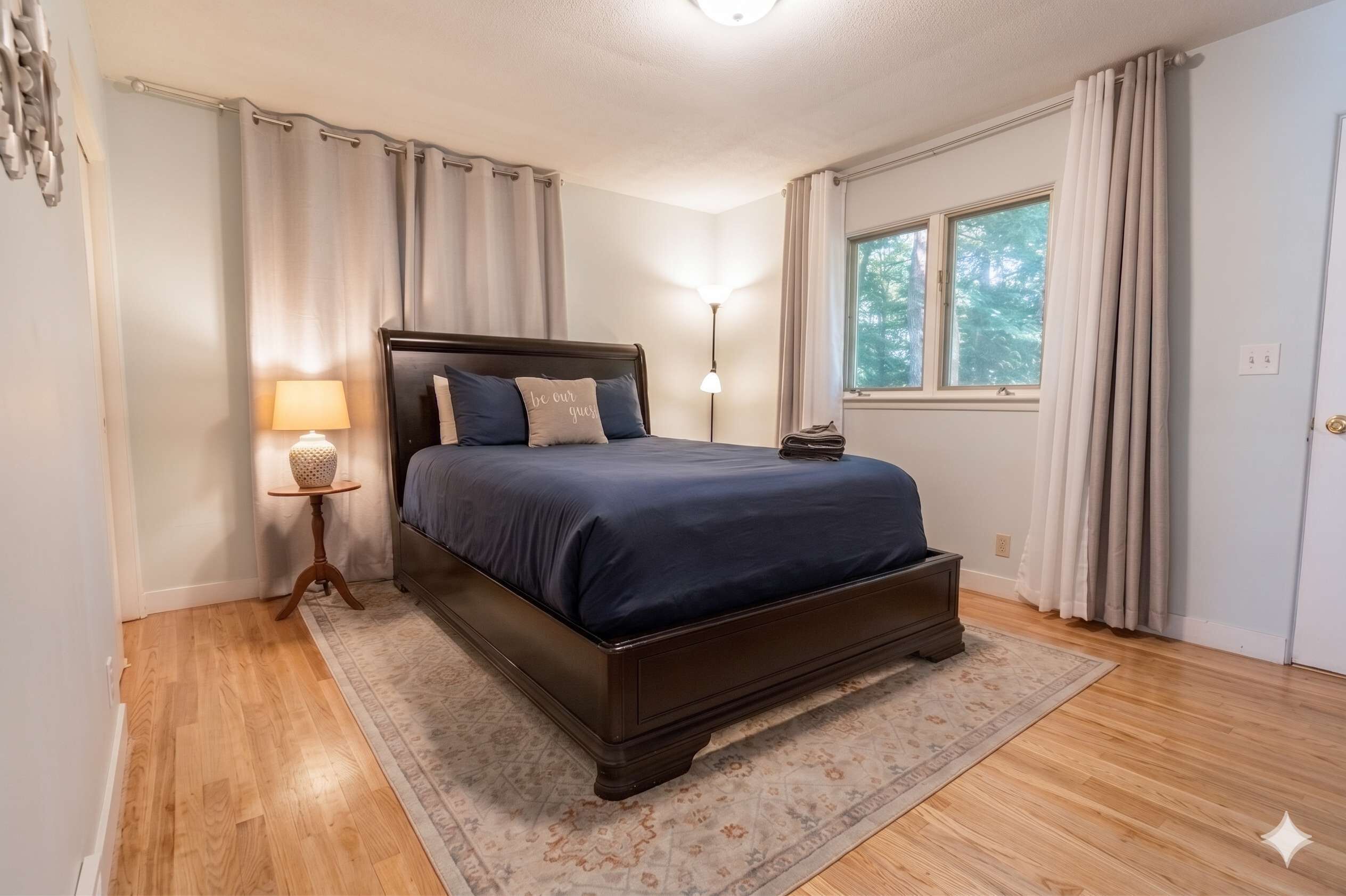 Une chambre à coucher avec un lit, une table de chevet avec une lampe, une fenêtre avec des rideaux et une porte.