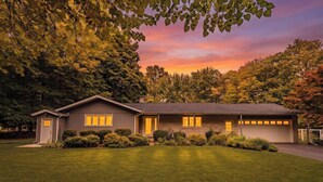 A single-story house with a garage, surrounded by well-maintained lawns and trees. - Stunning Ranch in the woods! (Berrien Springs)