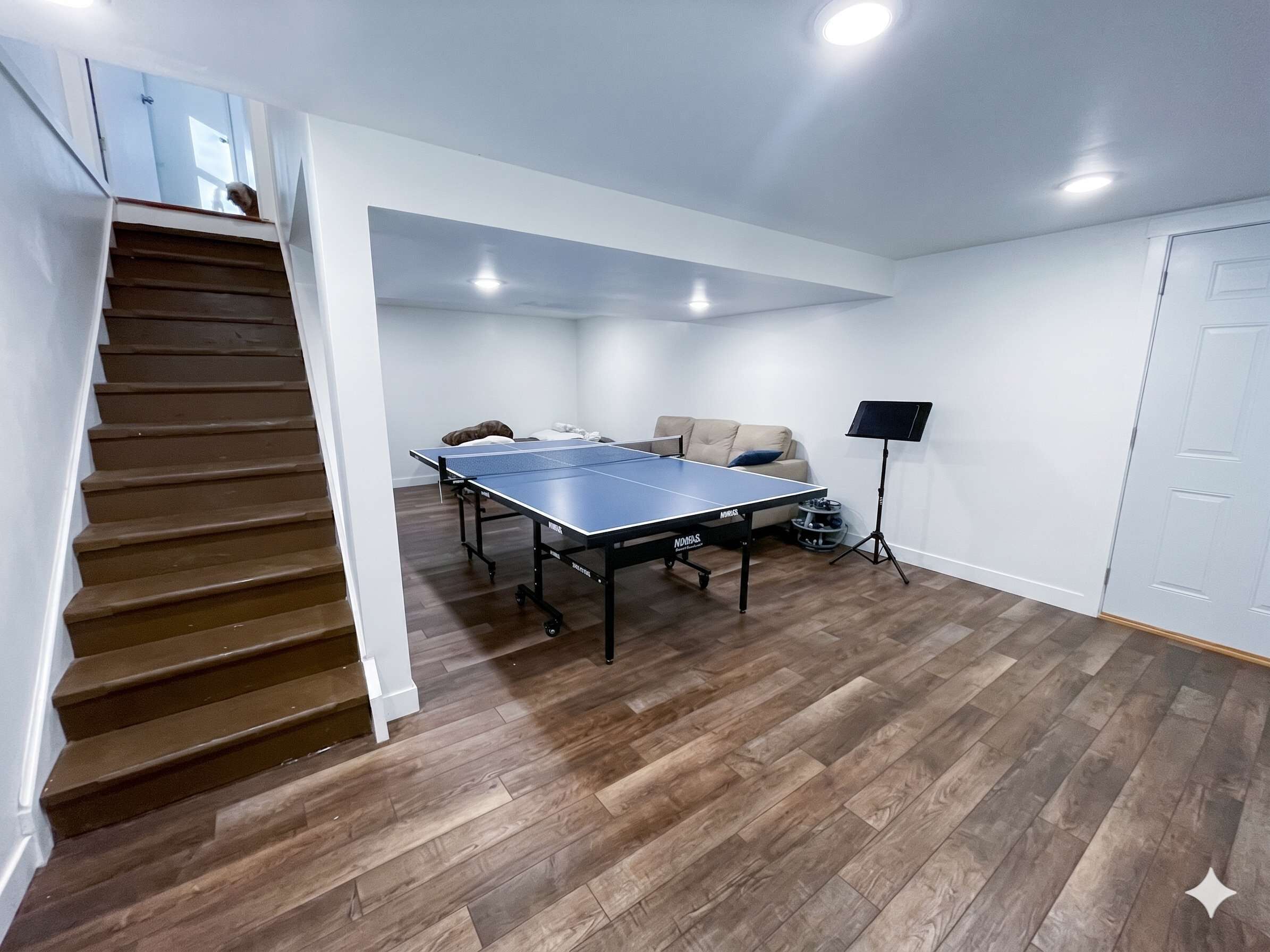 A room with a ping pong table, a sofa, a music stand, and a staircase.