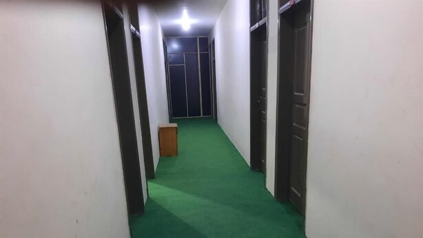 A hallway with green carpet, white walls, and doors on both sides. - Sada Bahar Inn Hotel (Gilgit)