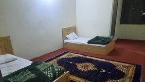 A room with two wooden beds, one with a green blanket and the other with a white pillow. A colorful rug is on the floor. - Sada Bahar Inn Hotel (Gilgit)