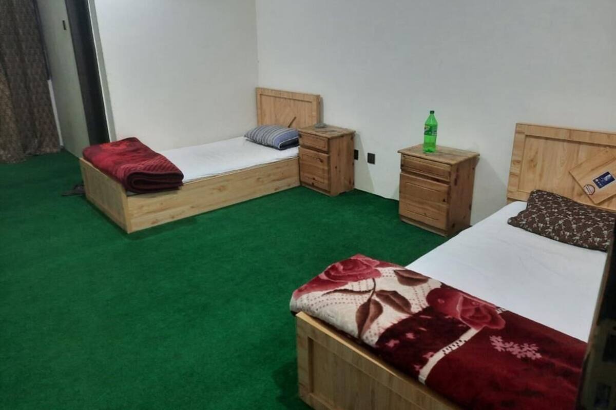 A room with two wooden beds, each with a pillow and a small wooden nightstand.