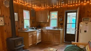 Een gezellig chalet binnen met een houtkachel, kitchenette en een bed.