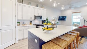 Una cocina moderna con armarios blancos, una isla central con taburetes de bar, un microondas y un bol con limones.