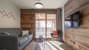 Una sala moderna con un sofá gris, un sillón negro y suelo de madera.