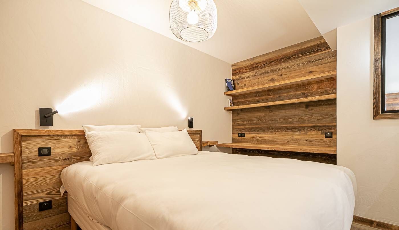 Quarto com cabeceira de madeira, cama com roupa de cama branca e estante embutida com acabamento rústico.