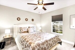 Une chambre à coucher avec un lit, un ventilateur de plafond, une fenêtre avec des stores et un tableau accroché au mur.