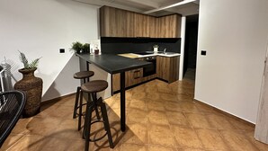 Una cocina moderna con encimera oscura, armarios de madera y salpicadero negro. Hay dos taburetes y una planta en maceta sobre la encimera.
