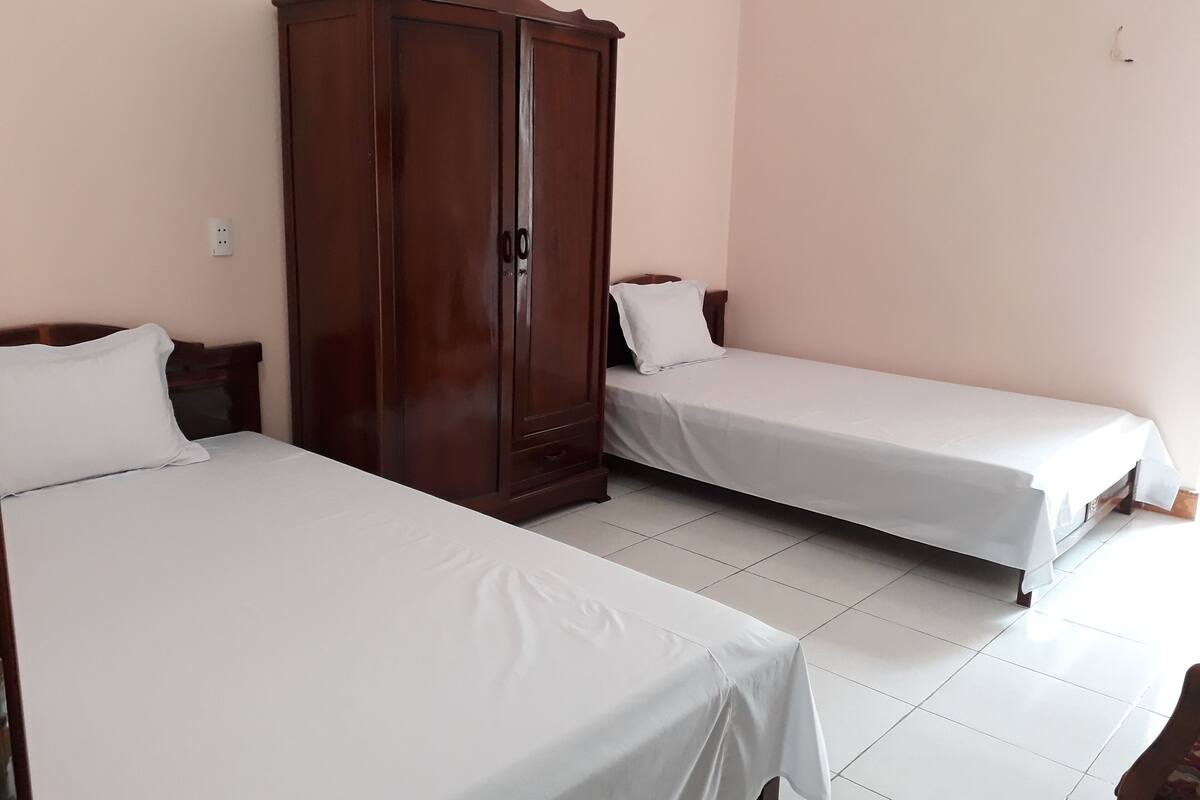 Une chambre avec deux lits simples, une armoire en bois et un sol carrelé de couleur blanche.