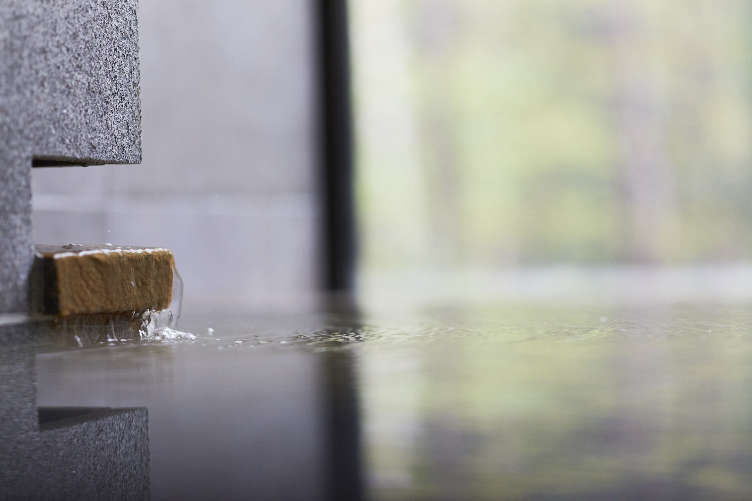 A close-up of a textured stone wall with a wooden object partially submerged in water.