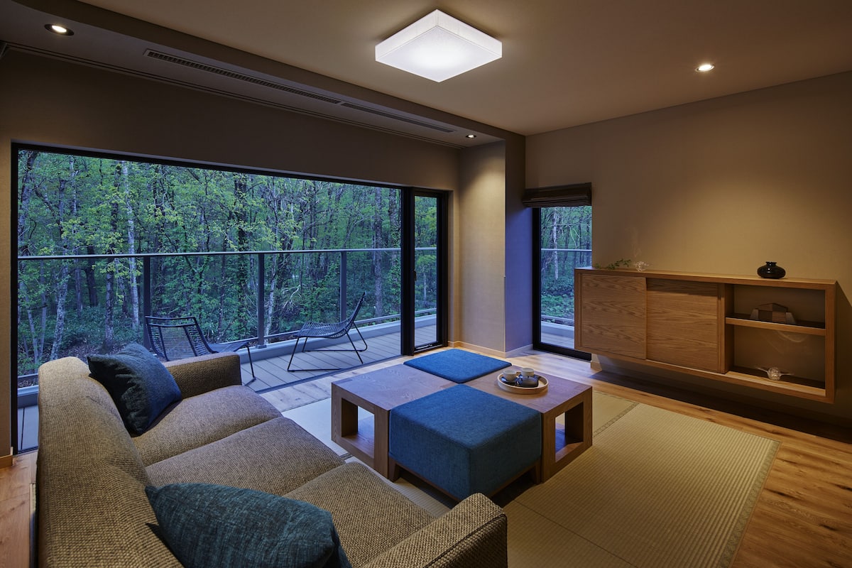 A modern living room with a large window, a sofa, a coffee table, and a wooden cabinet.