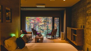 A modern bedroom with a large bed, two chairs, a small table, and a view of autumn foliage through a large window. - Okujozankeionsen Kashogyoen (Sapporo)