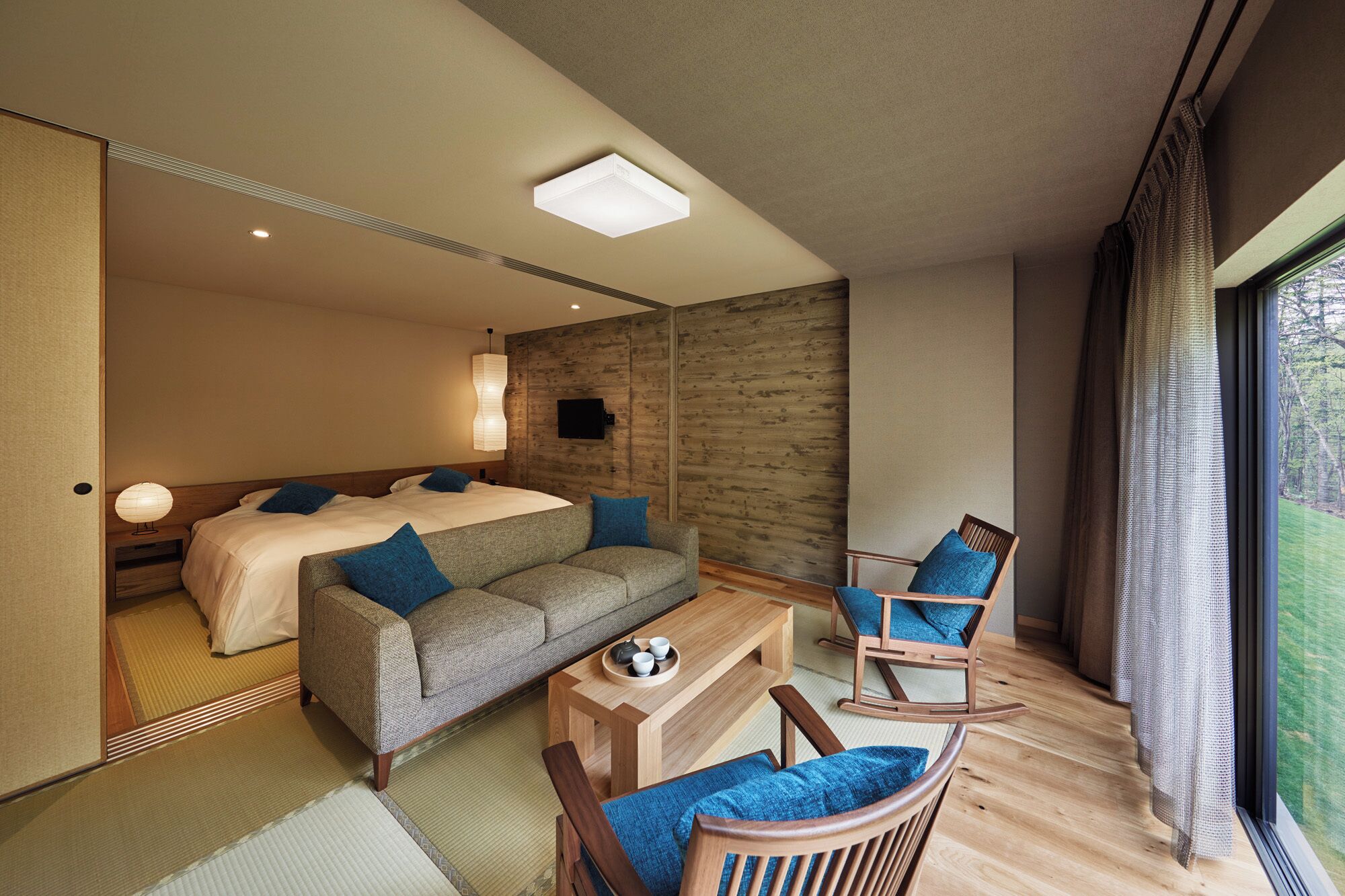 A modern hotel room with a large bed, a sofa, a wooden coffee table, and a chair.