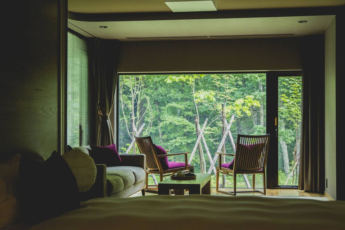 A bedroom with a large window, two chairs, a bed, and a small table.