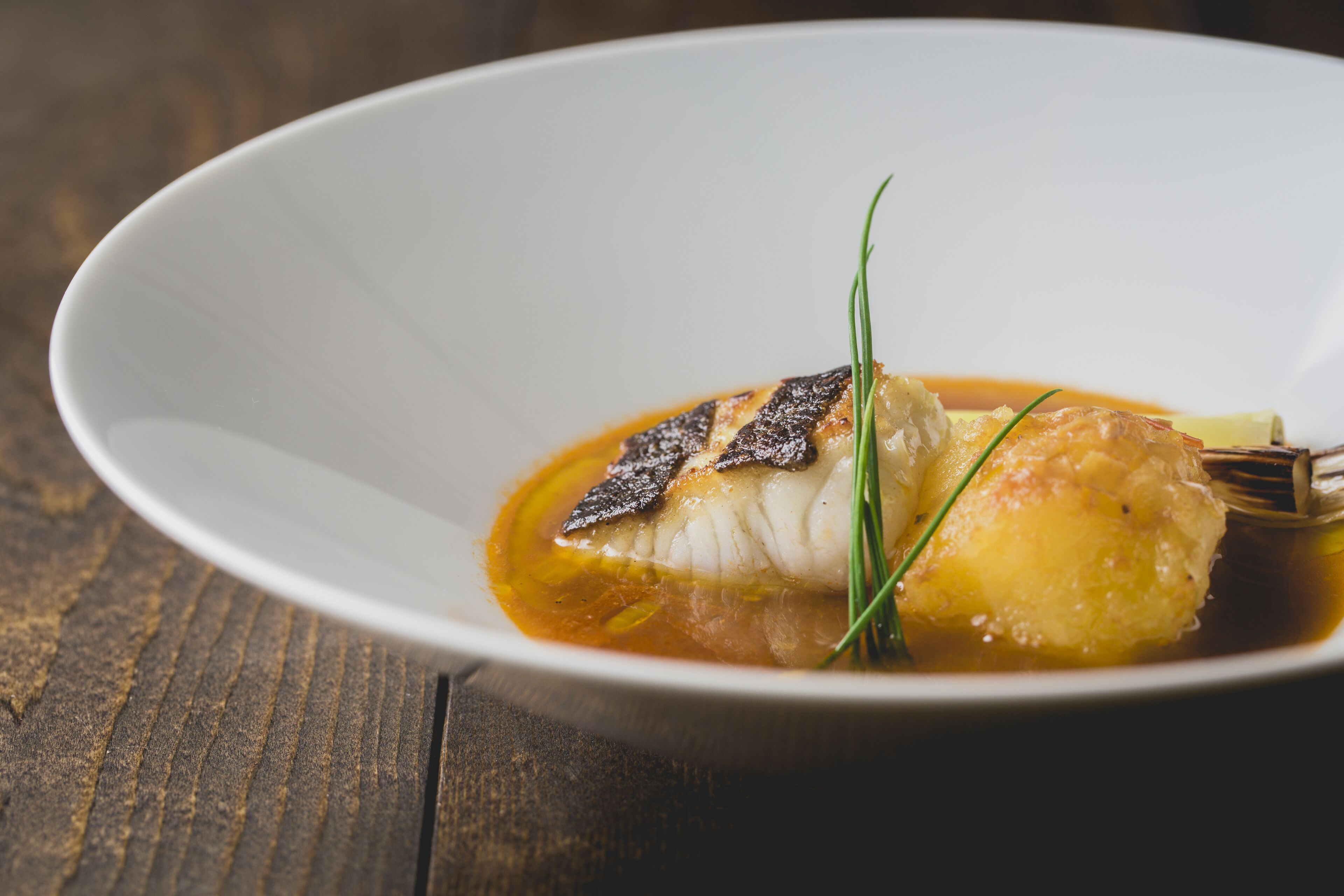 Un plato blanco con un trozo de pescado, guarnición y salsa.