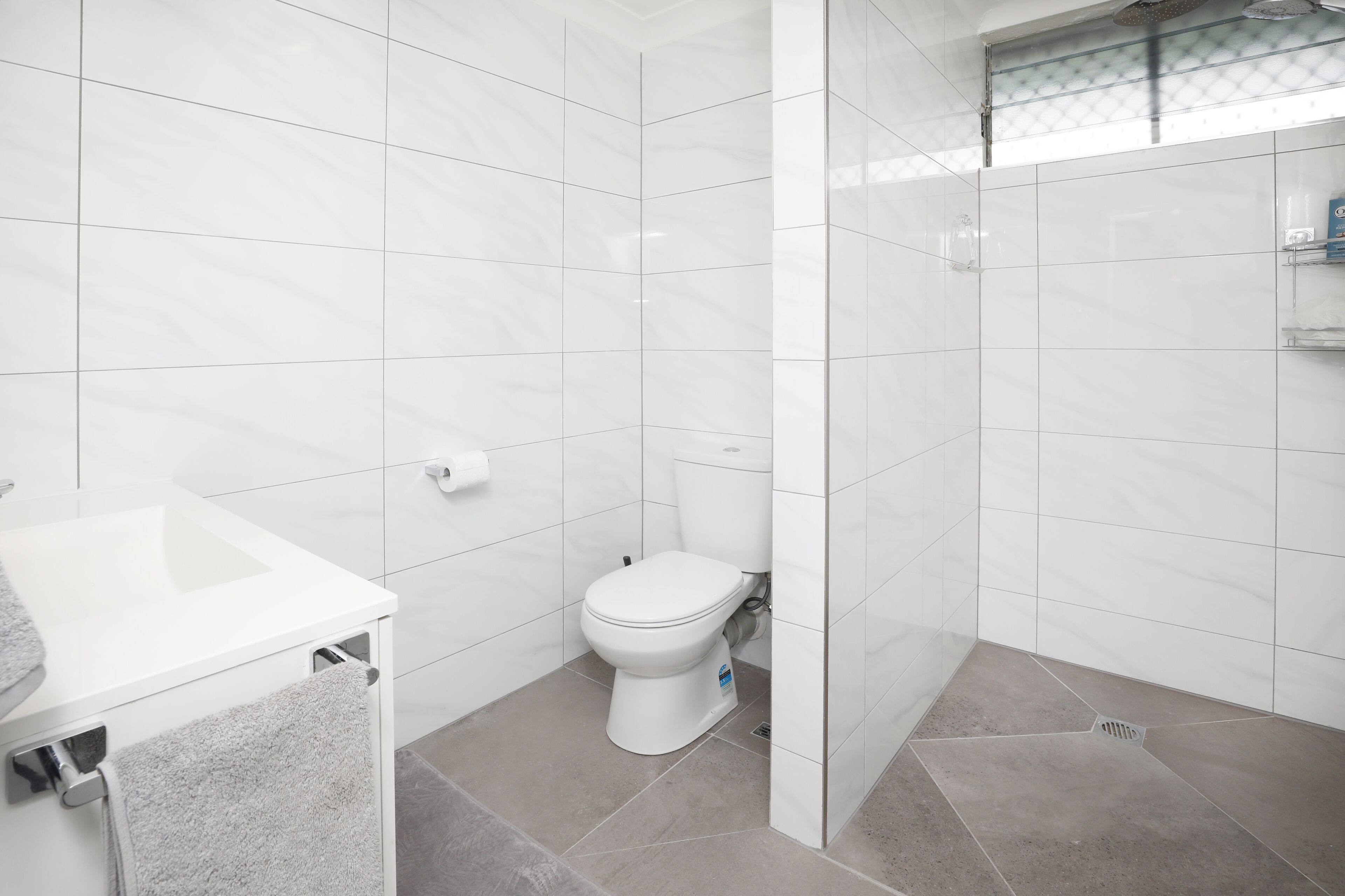 A bathroom with white tiles, a white toilet, a sink, and a shower area.