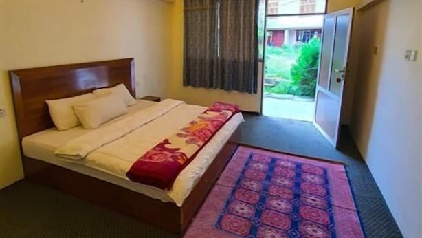 Una habitación de hotel con una cama, un ventanal con cortinas, una puerta y una lámpara en el techo.