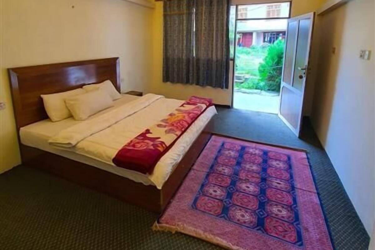 Quarto de hotel com cama, janela com cortinas, porta e luminária no teto.