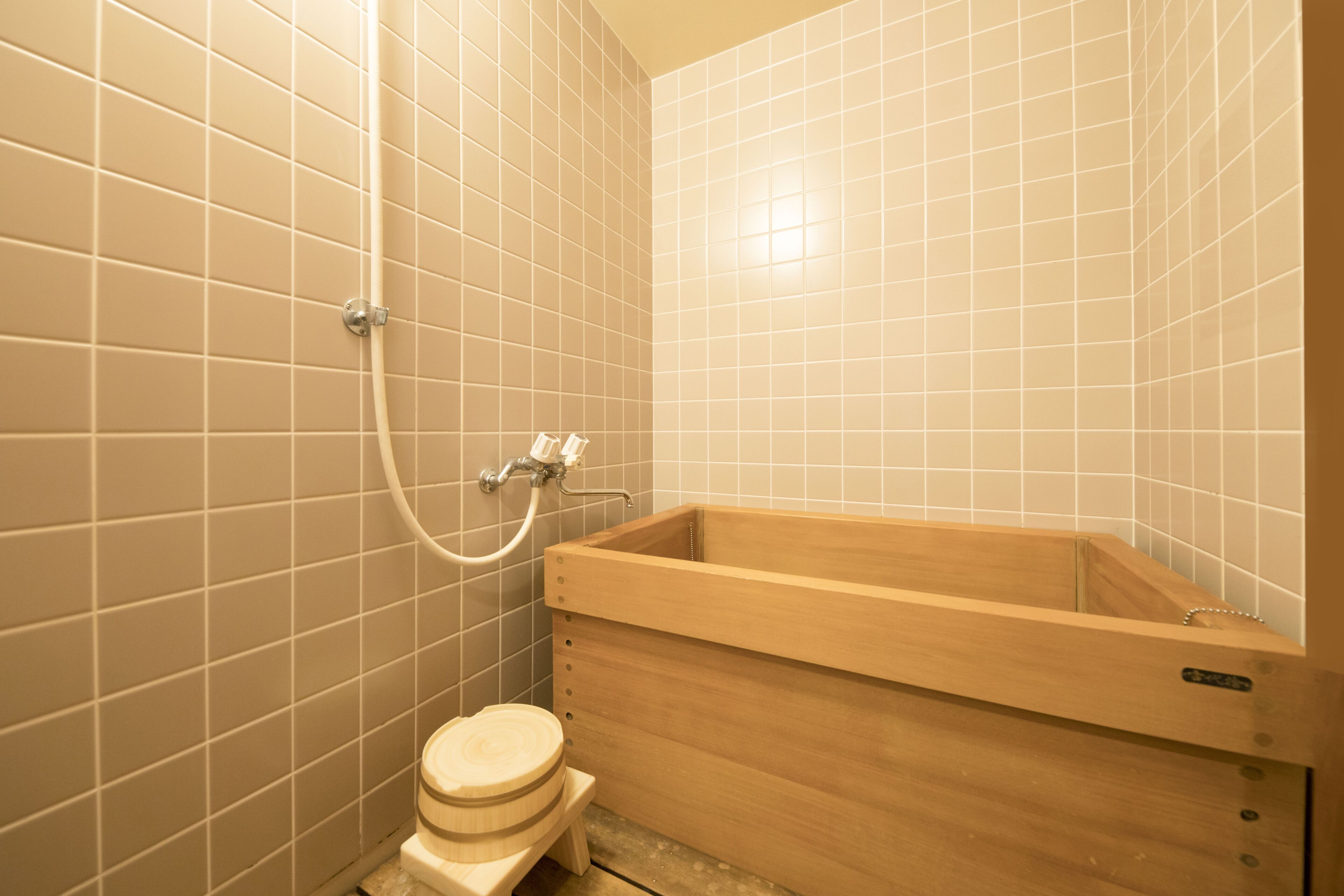 A small, modern bathroom with a wooden bathtub, a toilet, and tiled walls.