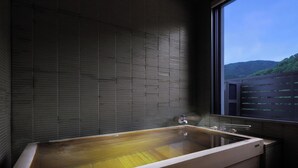 A wooden bathtub in a room with a view of a forested hill through a window. - bankokuya (Tsuruoka)