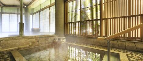 Un onsen japonés tradicional con un balneario de piedra, puertas correderas de madera y una escalera de madera.