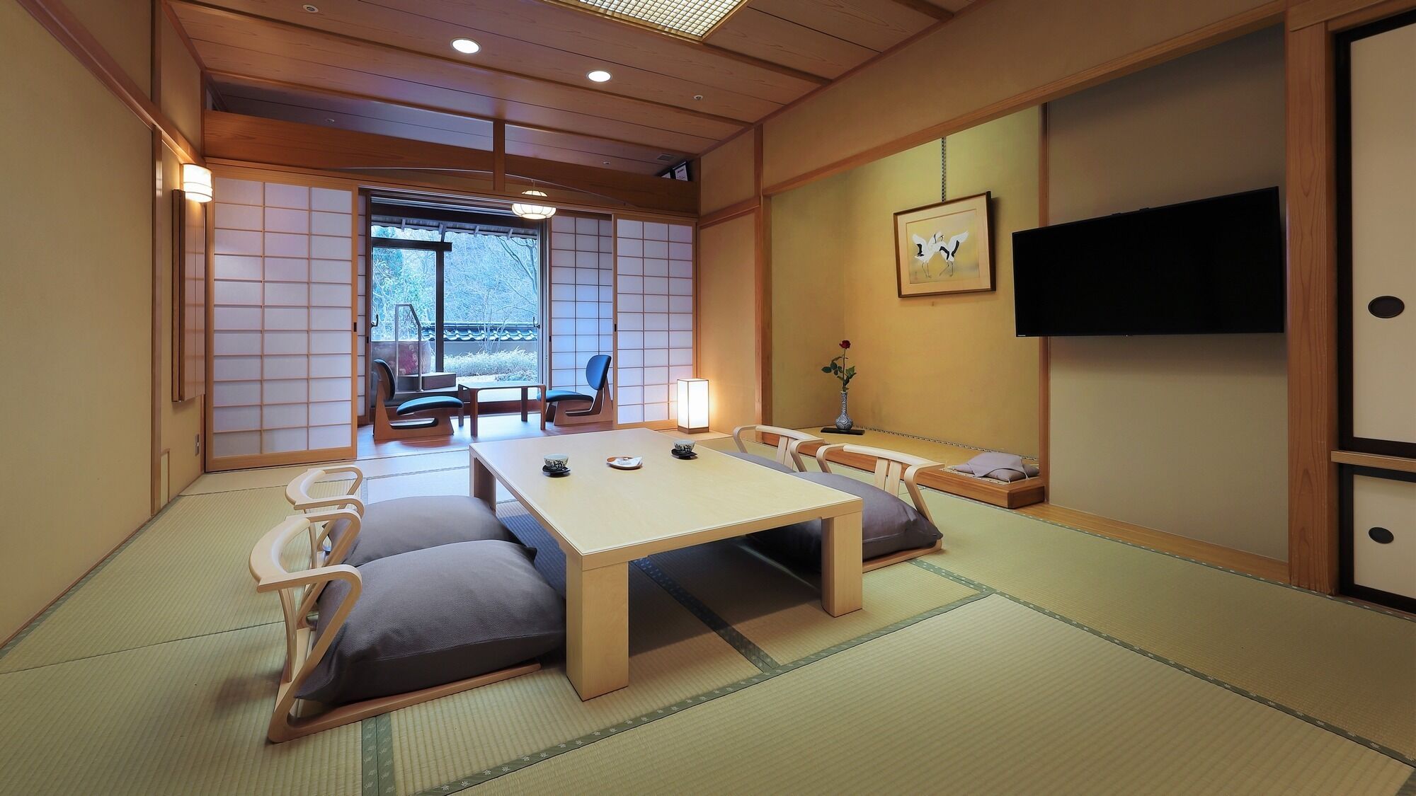Una habitación con esteras de tatami, una mesa baja, cojines, un televisor y una puerta corrediza que da a un balcón.