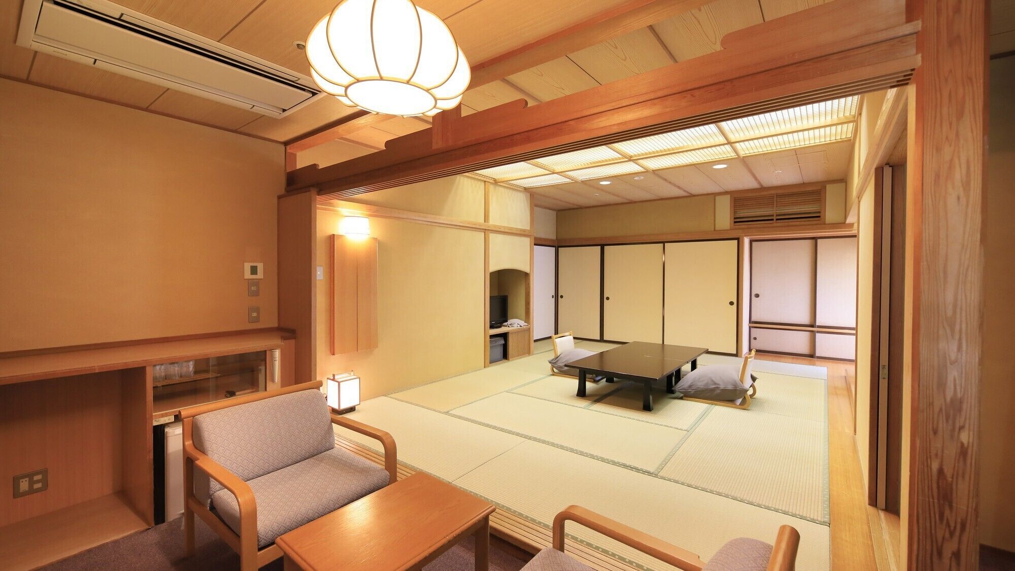 Una habitación de estilo japonés tradicional con suelo de tatami, una mesa baja, sillas y puertas correderas.