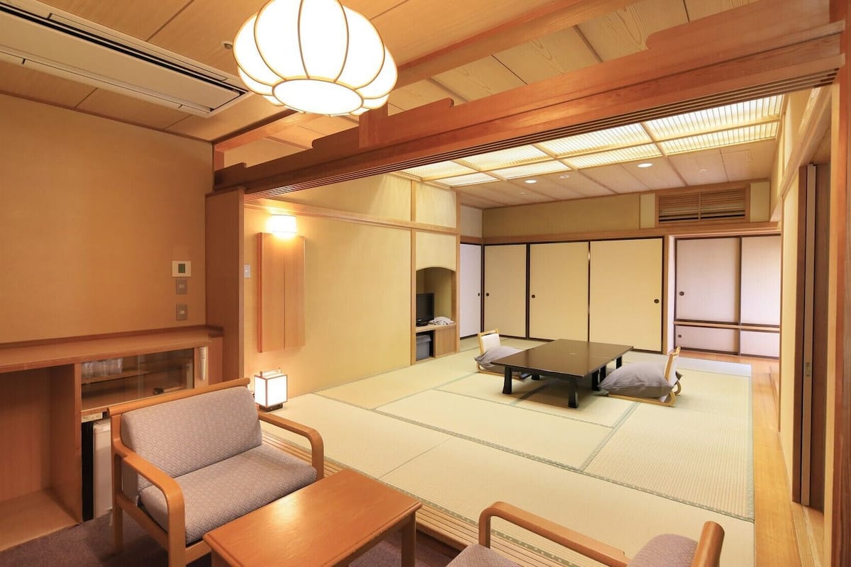 A traditional Japanese-style room with tatami flooring, a low table, chairs, and sliding doors.