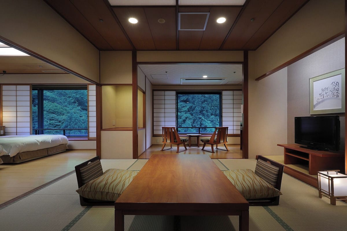 A traditional Japanese room with tatami flooring, a low table, and a television on a wooden stand.