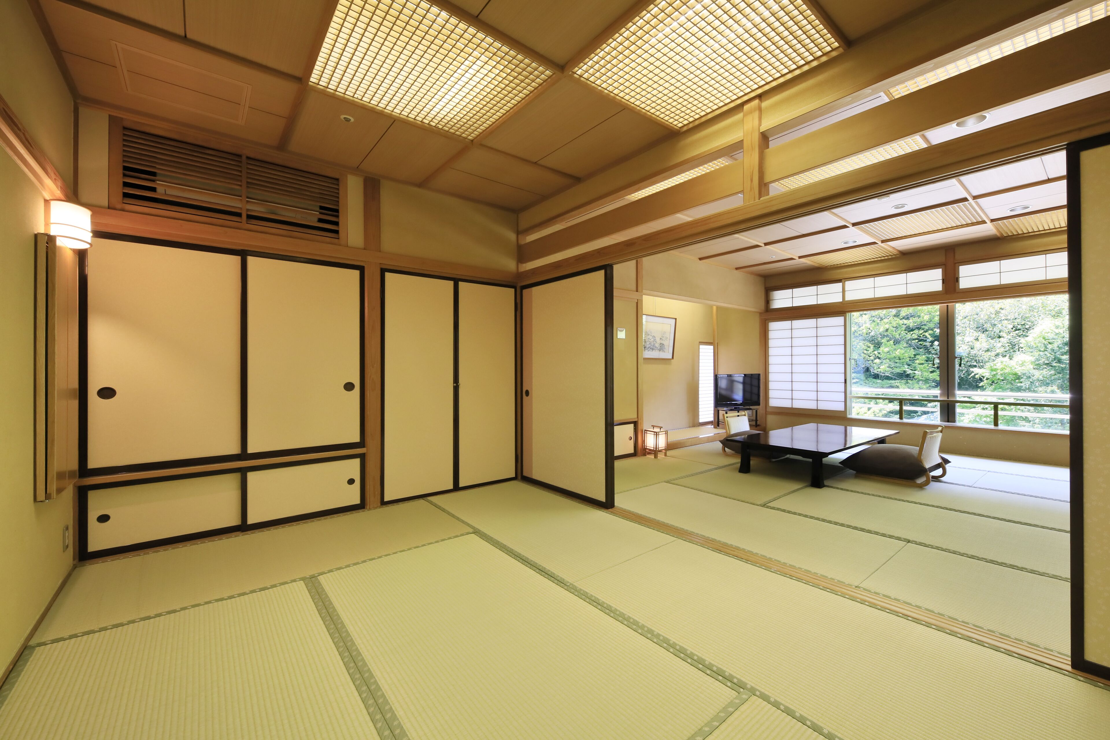 A traditional Japanese room with tatami flooring, sliding doors, and a view of greenery outside.