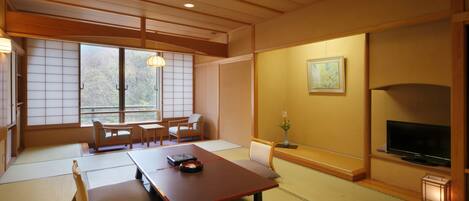 A traditional Japanese room with tatami flooring, a low table, cushions, a television, and sliding doors.