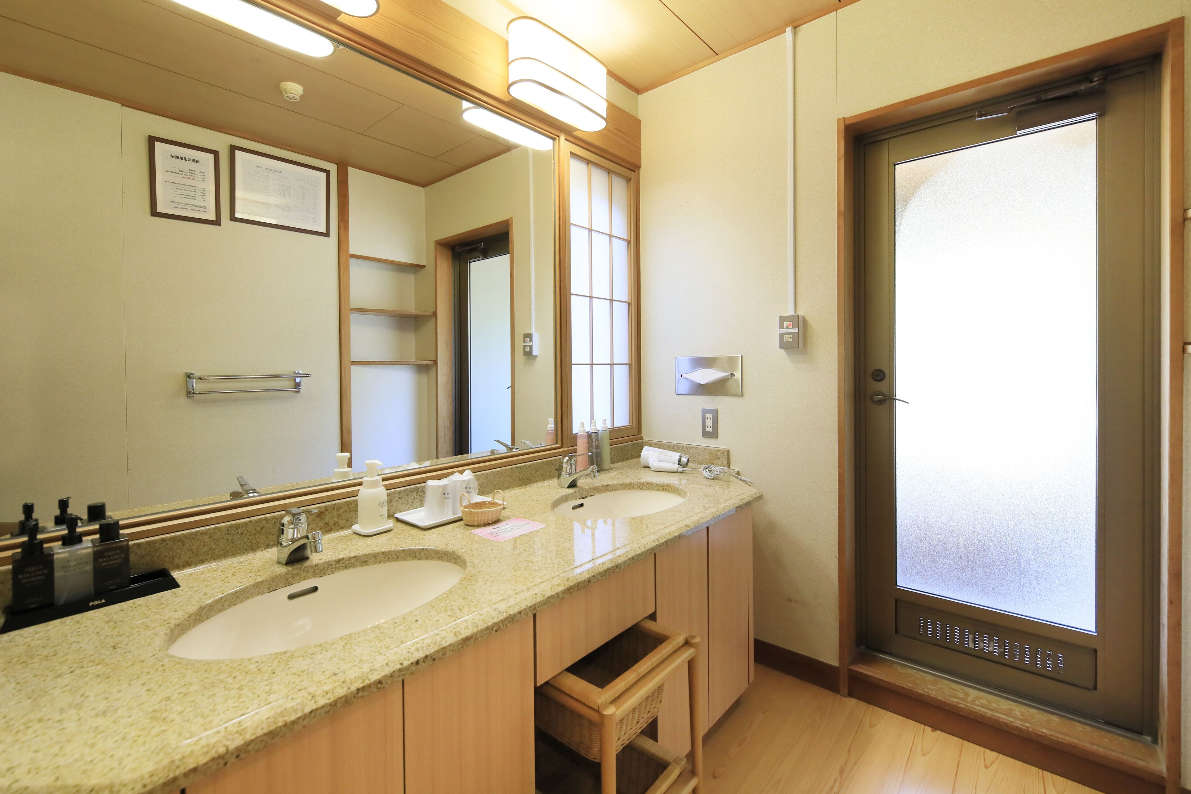 A hotel bathroom with two sinks, a large mirror, and a frosted glass door.