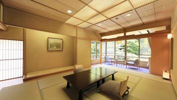 A traditional Japanese room with tatami flooring, a low table, and a view of a garden through large windows.