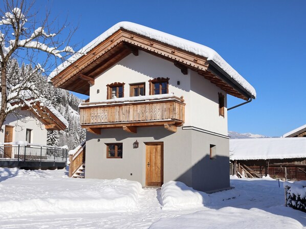 A two-story chalet with a balcony, wooden railings, and a snow-covered roof.