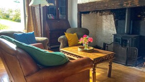 A cozy living room with a fireplace, leather sofa, and a table with a vase of flowers.